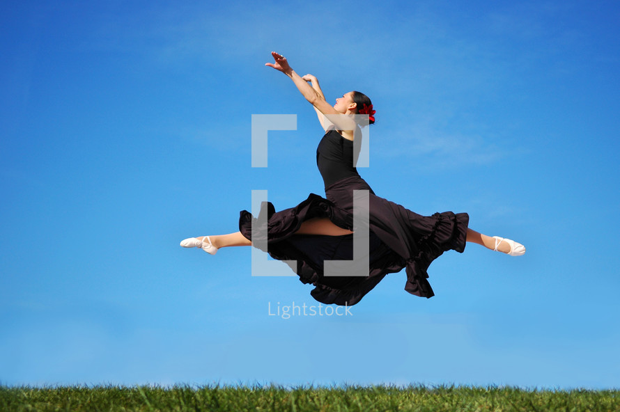 Ballerina leaping in a field of grass.