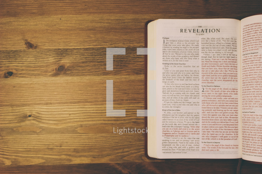 Bible on a wooden table open to the book of Revelation.