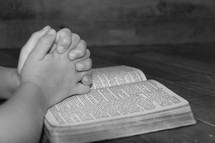 praying hands on the pages of a Bible 