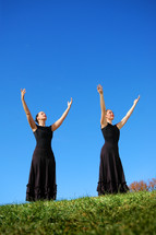 Two woman, on a hillside, with their arms raised