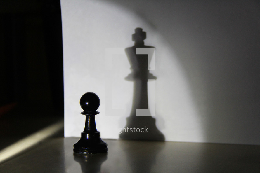 Light shining on a chess pawn, casting a shadow of a king chess piece.