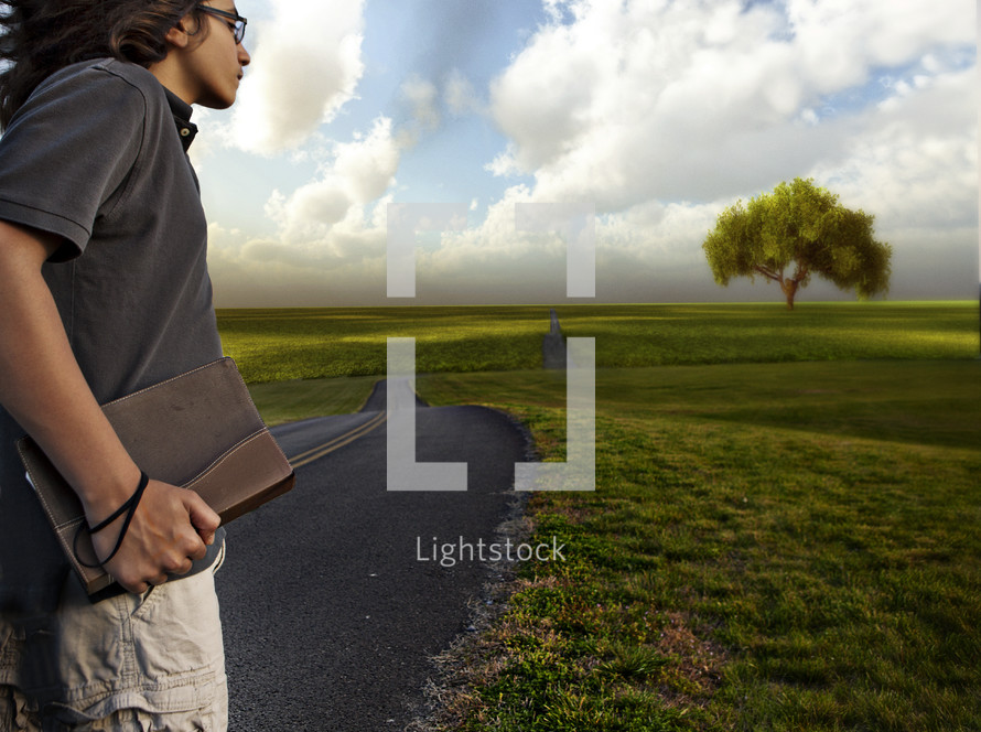 teen boy holding a bible heading down the open road