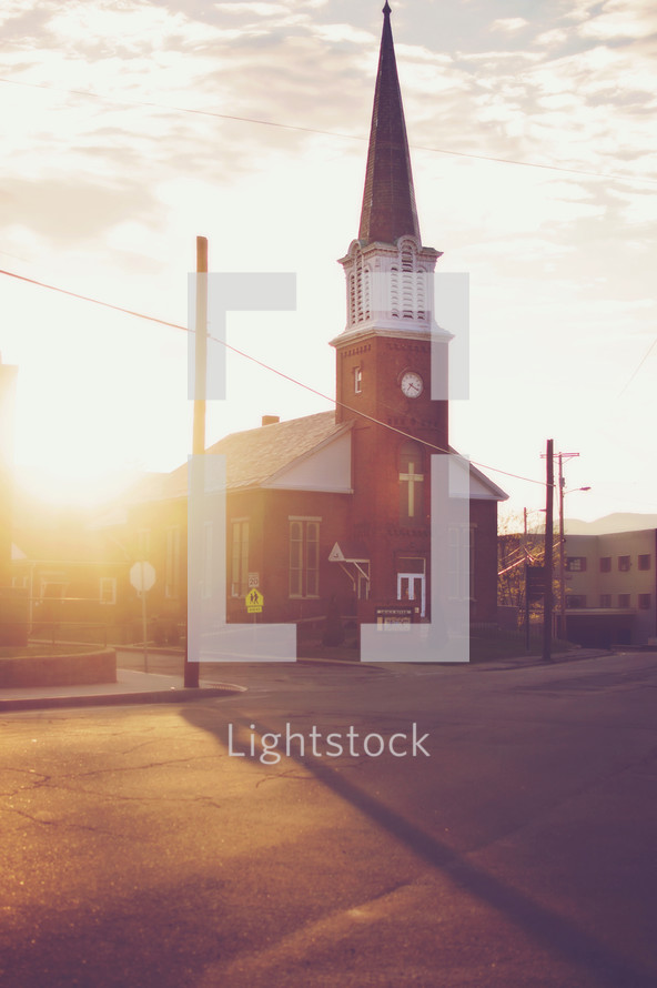 Sun shining behind a church with a tall steeple.