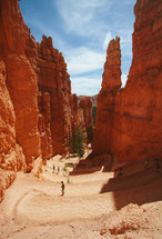 people walking downhill in a canyon and red rock peaks 