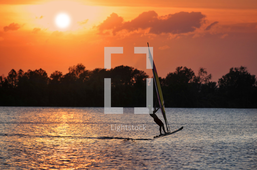 Silhouette of a windsurfer on a lake at sunset.