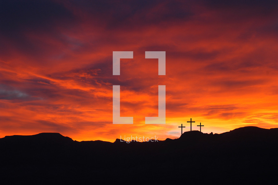 Silhouette of three crosses on a hill with a red sunrise sky