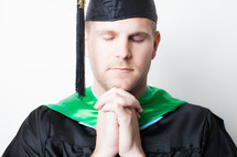 Graduate with hands clasped in prayer.