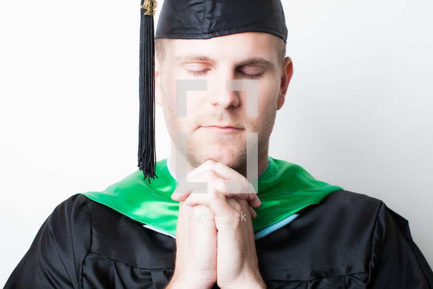 Graduate with hands clasped in prayer.