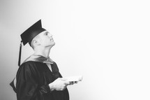Graduate holding a Bible and looking up with eyes closed in prayer.