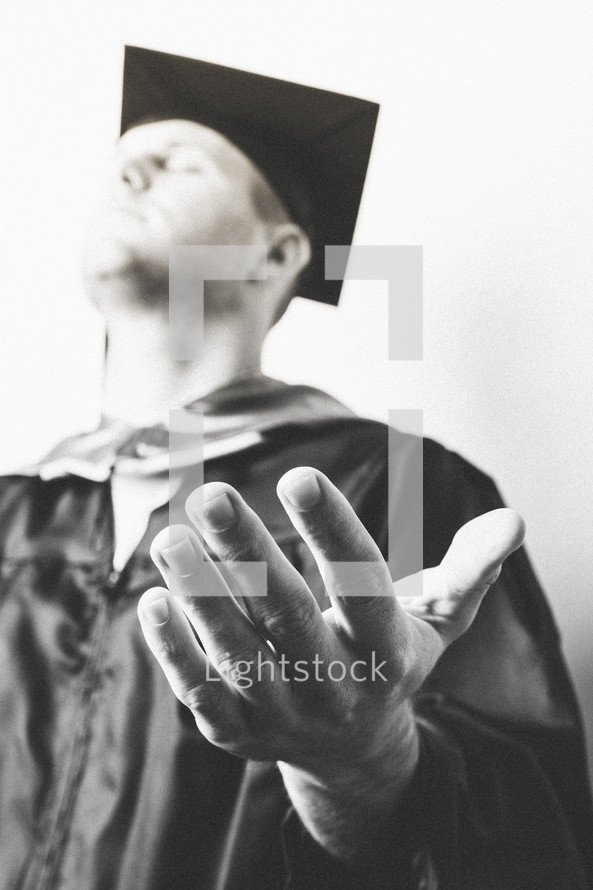 Graduate with hands extended in prayer.