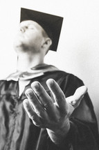 Graduate with hands extended in prayer.