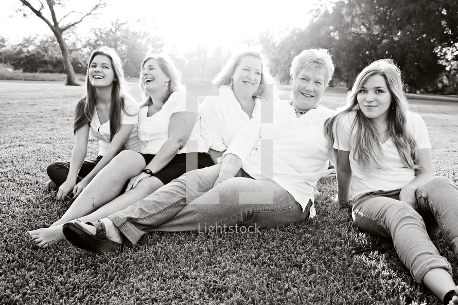Five women sitting together on a grassy lawn.