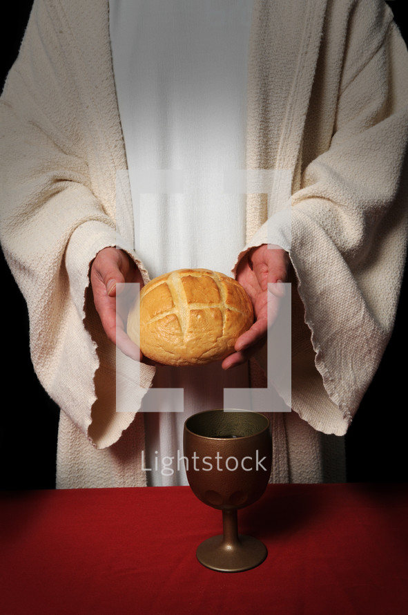 Priest hold a loaf of bread with a goblet of wine on the table