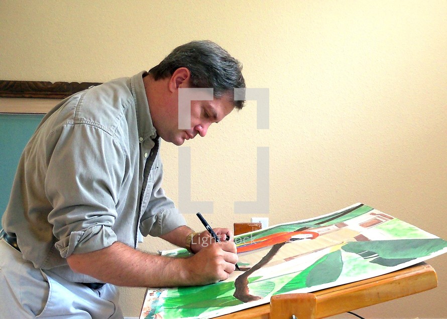 A male Artist paints intently at his easel working on a new painting.