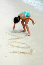 girl drawing the word love in the sand 