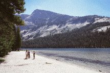 men standing on a beach near a lake and mountain peak 