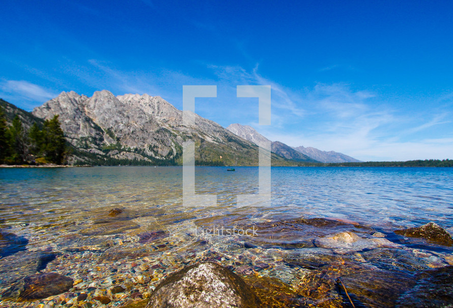 rocks along a  lake shore and mountains