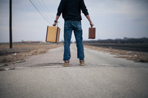 man holding out suitcases standing in the middle of a road