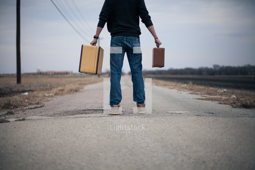 man holding out suitcases standing in the middle of a road