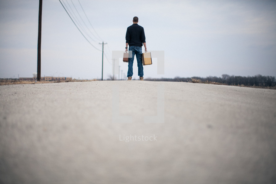 man walking down the middle of a road carrying suitcases
