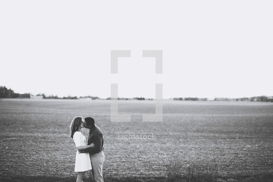 a couple kissing in a plowed field 
