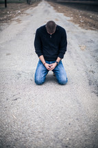 man kneeling in prayer in the middle of a road