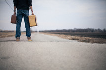man holding suitcases looking down a long road