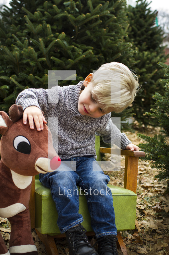 a boy child petting a stuffed Rudolph in a Christmas tree farm 