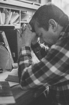 a man sitting at a desk praying and reading a Bible 