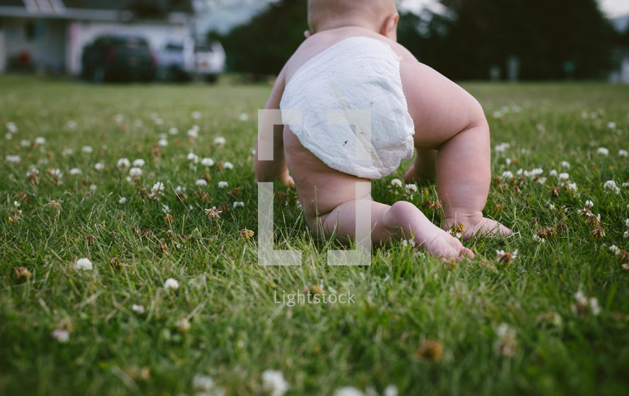 Infant in a diaper crawling in the grass.