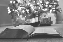 open Bible and gifts under a Christmas tree 
