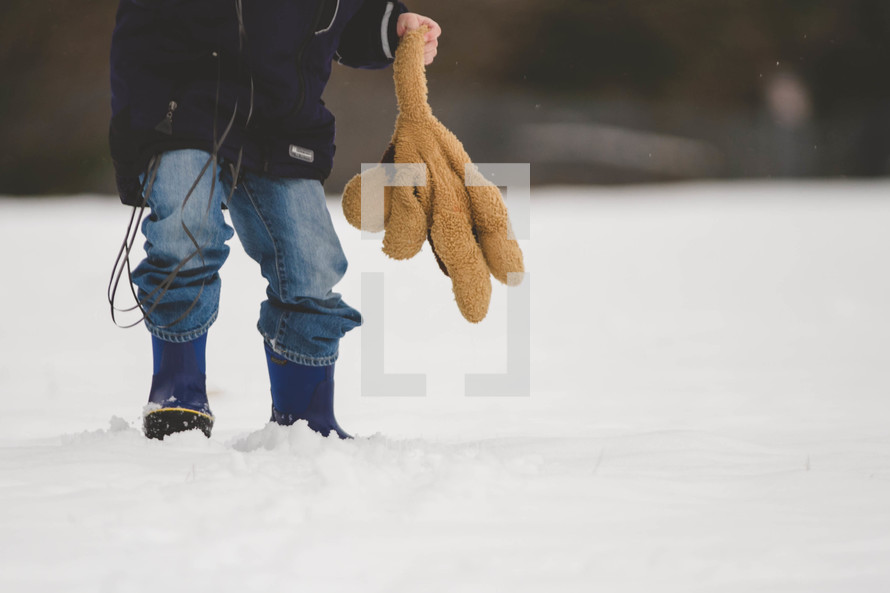boy child walking in the snow holding a teddy bear 