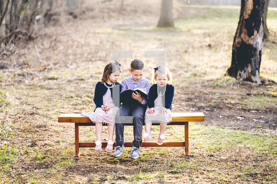 siblings sitting on a bench outdoors reading a Bible together 
