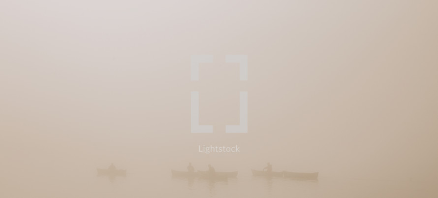 people on boats on a lake in dense fog 