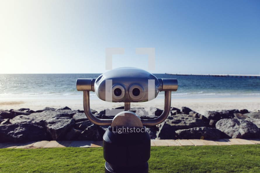 A robot standing before a rocky oceanside.