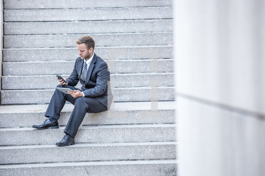 a businessman with a tablet and cellphone sitting on steps 