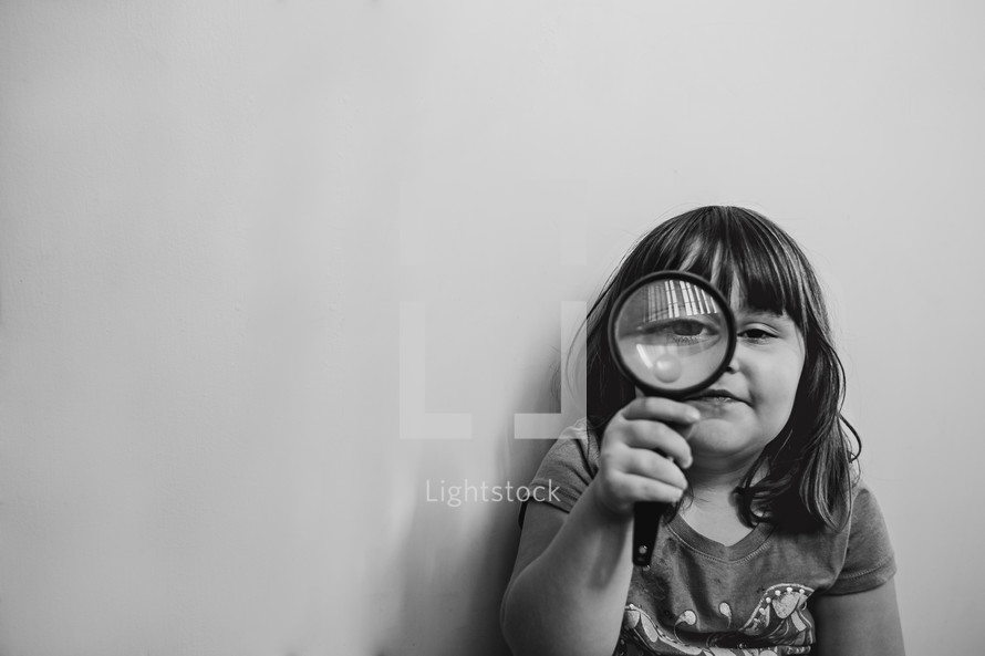 a girl child looking through a magnifying glass 