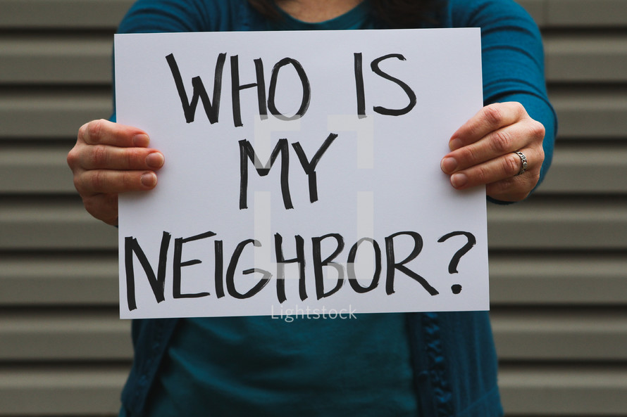 A woman holding a sign that says who is my neighbor? 