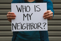 A woman holding a sign that says who is my neighbor? 