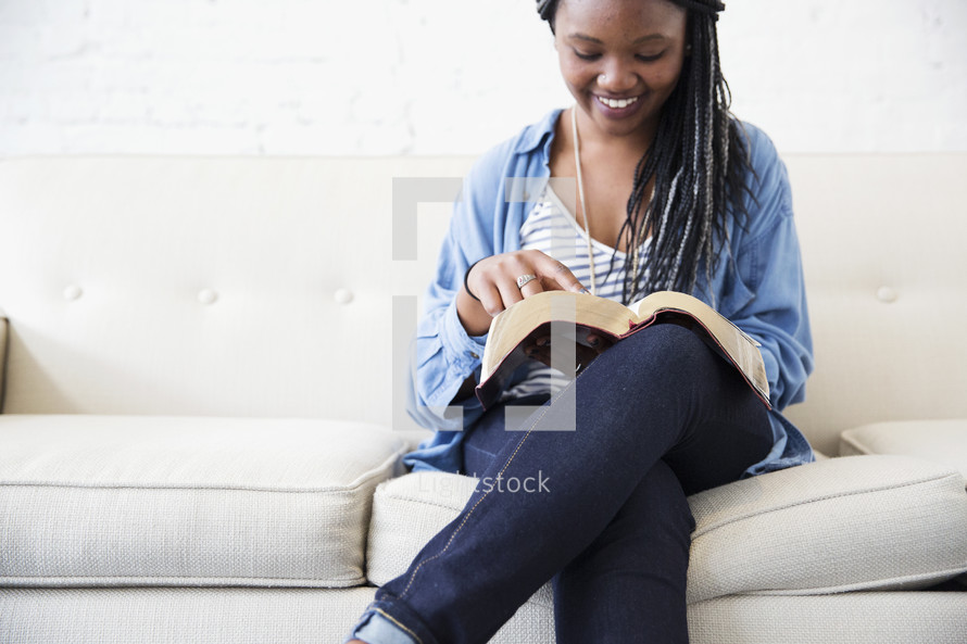 a young woman sitting on a couch reading a Bible.