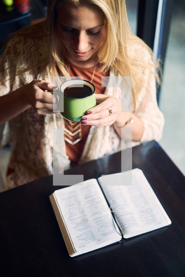 a woman reading a Bible and drinking coffee in a coffee shop 