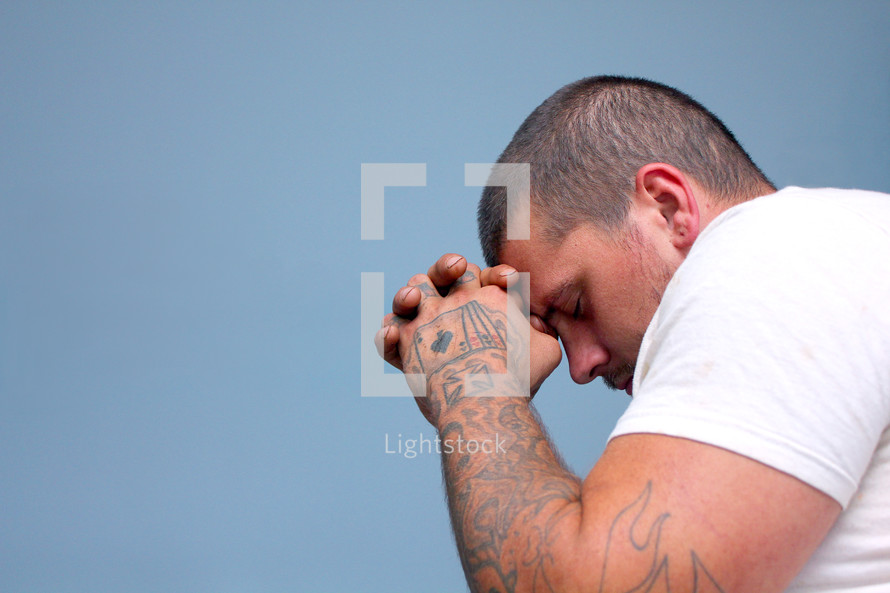 man with tattooed hands praying 