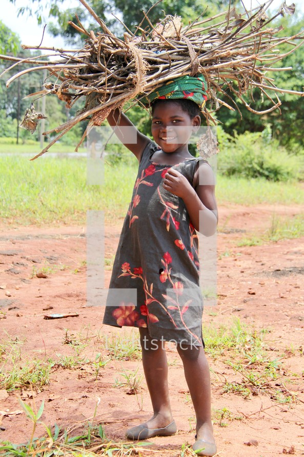A little African girl carrying a bundle of sticks on her head 