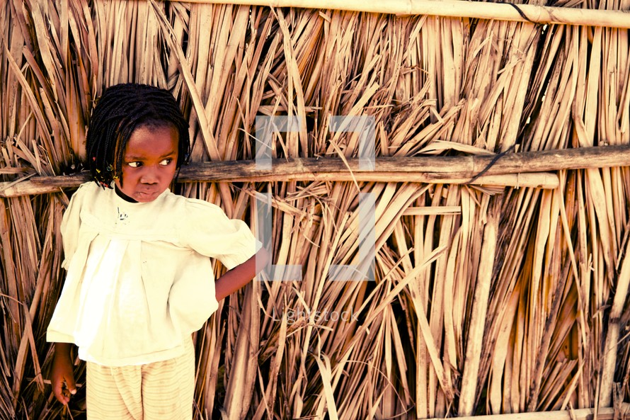 toddler girl leaning against a hut 