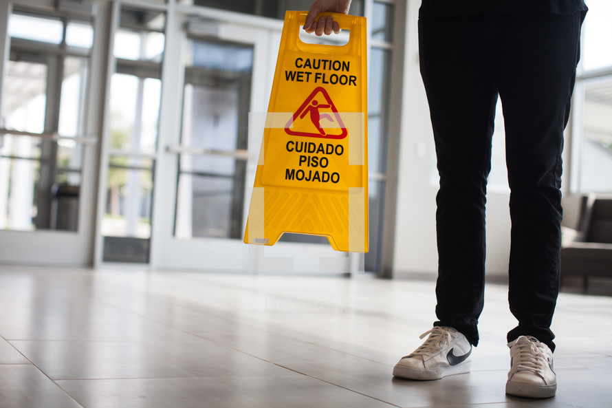 man in a lobby putting down a wet floor sign 