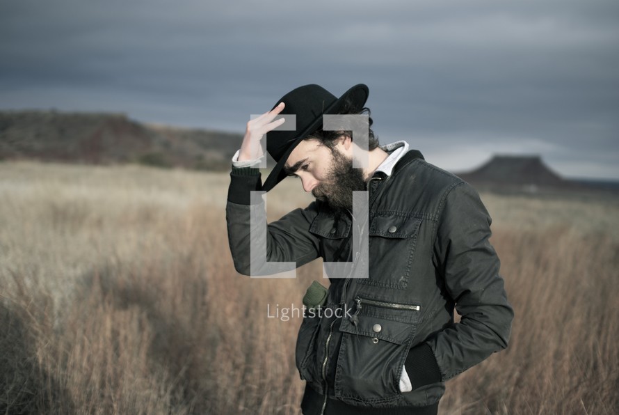 man with a black hat standing in a field alone 