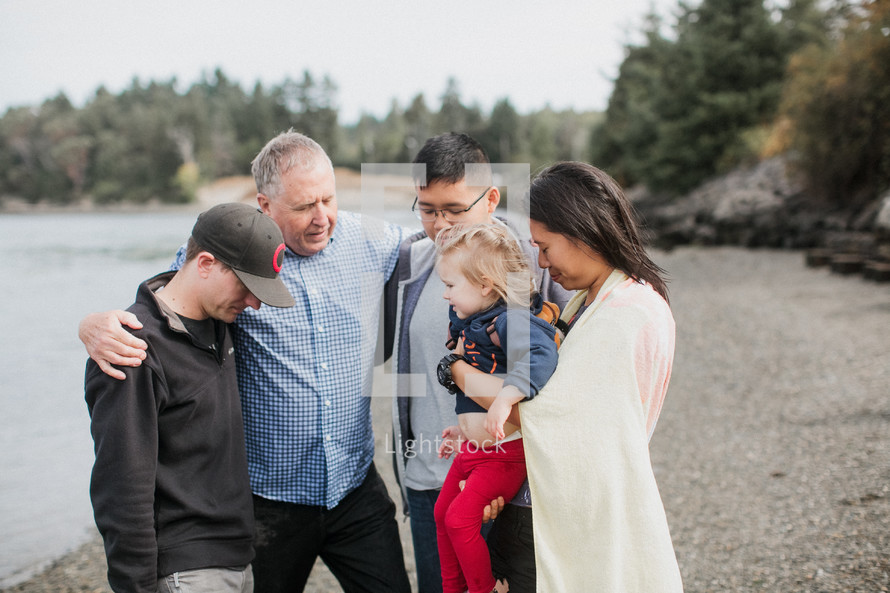 a pastor praying with a family before a baptism in a river outdoors 