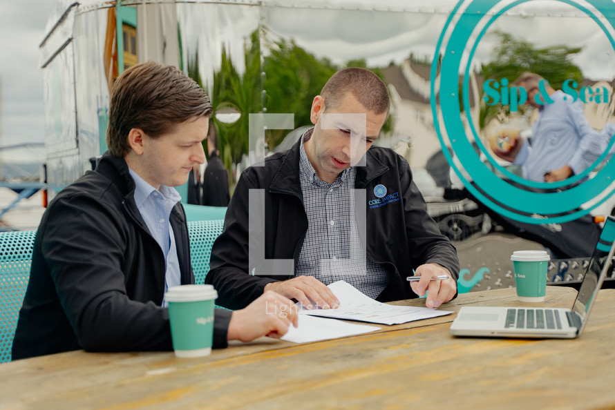 two men sitting at a coffee shop working 