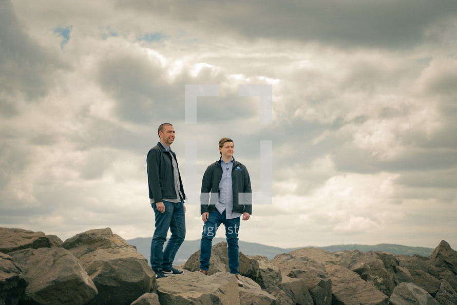 two men standing on rocks on a mountaintop 