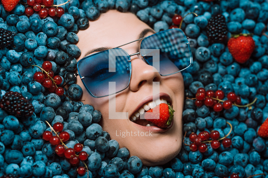 Happy woman face in eyewear fresh ripe berries - blueberries, strawberries